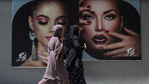 Mujeres vestidas con burka pasan junto a una valla publicitaria colocada en la pared de un salón de belleza en Kabul el 7 de agosto de 2021. (SAJJAD HUSSAIN / AFP).