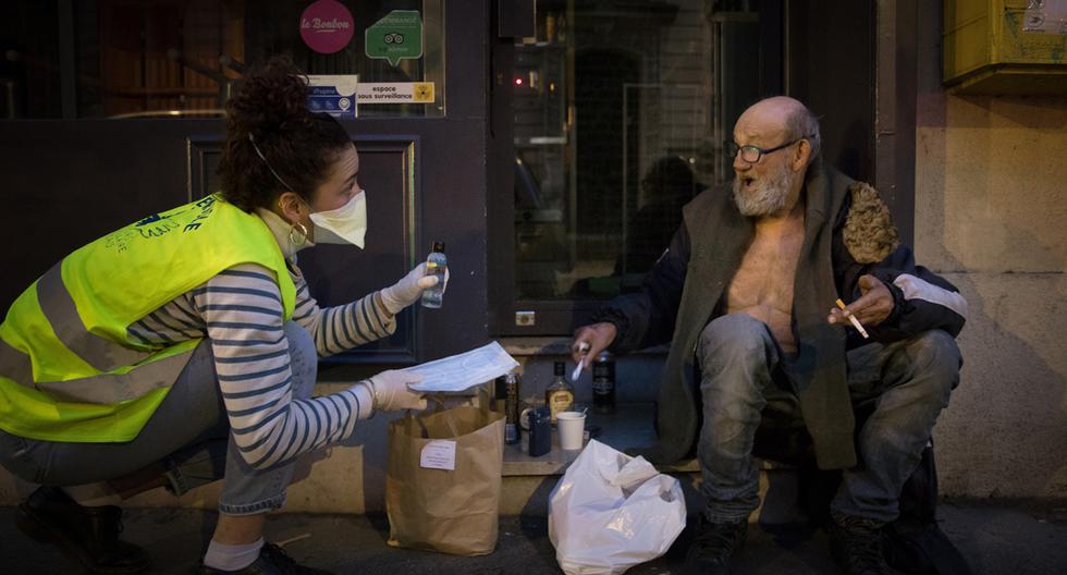 Imagen referencial. Un voluntario de la organización benéfica Secours Populaire con máscara y guantes le da un desinfectante de manos y varios artículos a las personas sin hogar en la calle en París. (AFP/Joel Saget).