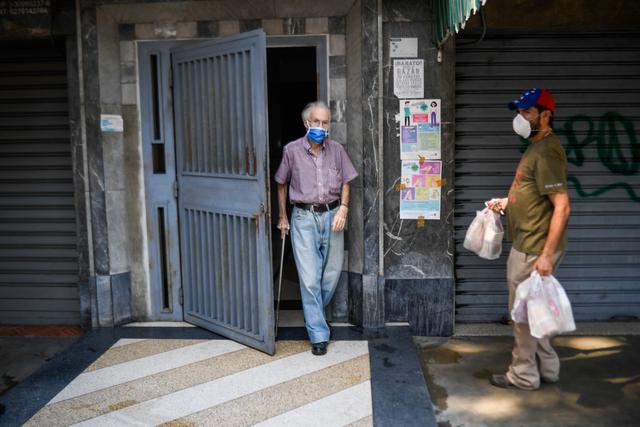Un voluntario entrega una bolsa de comida a un anciano como parte del "Plan del Buen Vecino", en Caracas, en medio del bloqueo destinado a detener la propagación del nuevo coronavirus. (Foto: AFP/Federico Parra)
