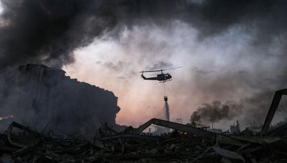 Un helicóptero apaga un incendio en el lugar de la explosión en el puerto de Beirut, la capital del Líbano. (AFP/STR)