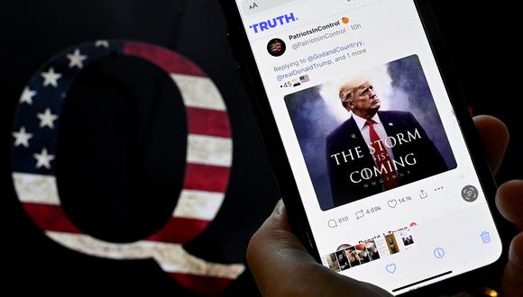 En esta ilustración fotográfica, la cuenta TRUTH Social de Donald Trump se ve en un dispositivo móvil con una imagen de una calcomanía de QAnon en el fondo en Washington, DC el 13 de septiembre de 2022. (Foto de OLIVIER DOULIERY / AFP)