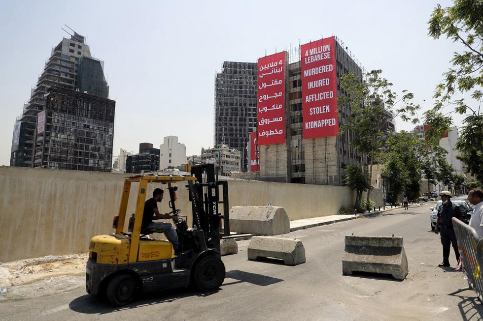 Un camión bloquea una carretera que conduce a la carretera que da al puerto de Beirut con pancartas colgadas en un edificio dañado durante la explosión del puerto del año pasado al otro lado de la calle, como lo marca Líbano el 4 de agosto de 2021, un año desde que una explosión catastrófica devastó la capital Beirut. (Foto de JOSEPH EID / AFP)