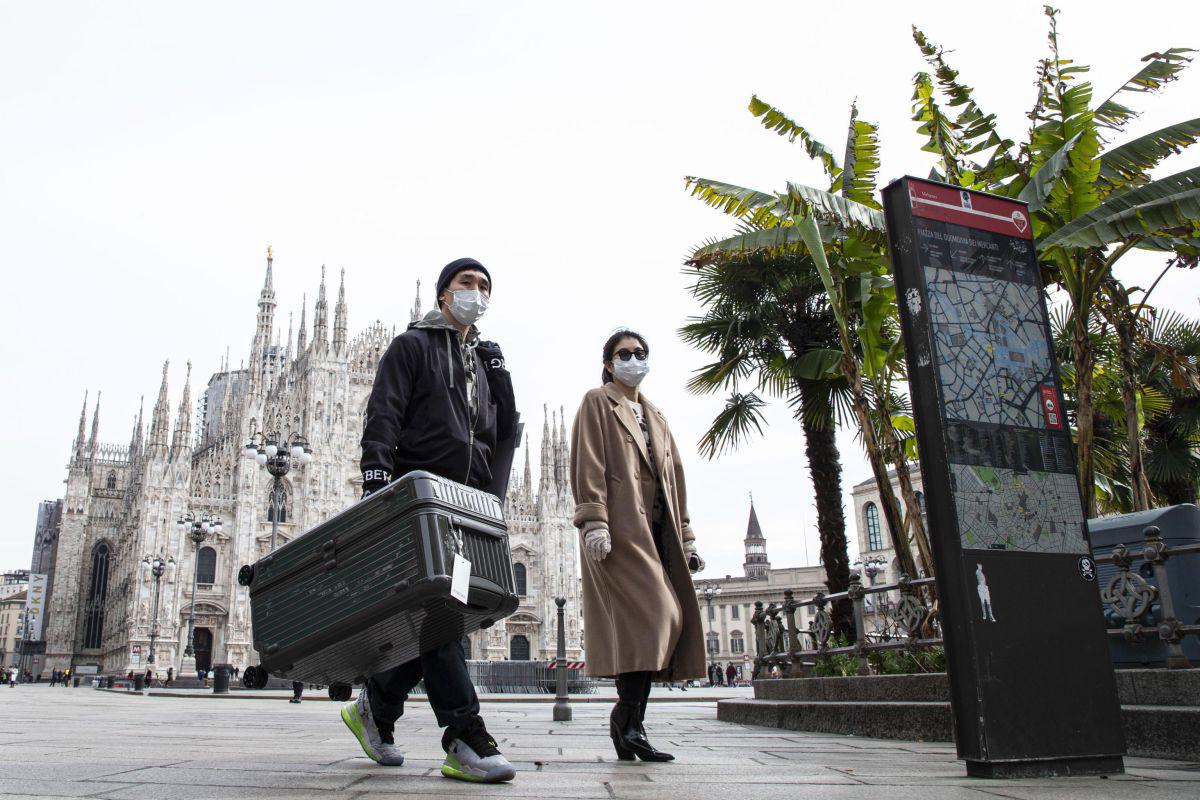 Los turistas usan máscaras faciales protectoras mientras caminan por la casi vacía Piazza del Duomo ('Plaza de la Catedral') en Milán, Italia. (EFE).