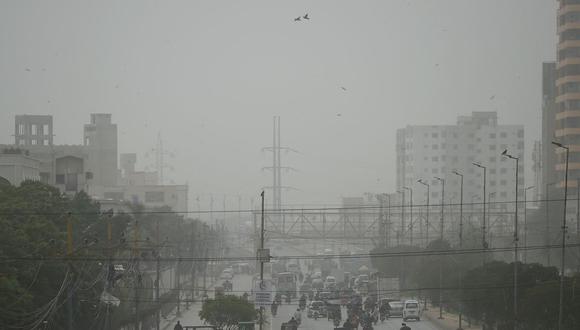 Los viajeros se abren camino en medio de una atmósfera polvorienta a lo largo de una calle transitada durante un día ventoso en Karachi el 22 de enero de 2022. (Foto de Rizwan TABASSUM / AFP)