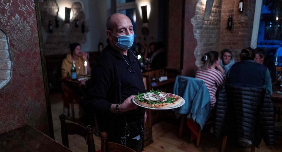Imagen referencial. Un camarero, que usa una máscara facial por el coronavirus, sirve una pizza en Pepenero, un restaurante italiano en Alemania. (AFP / John MACDOUGALL).