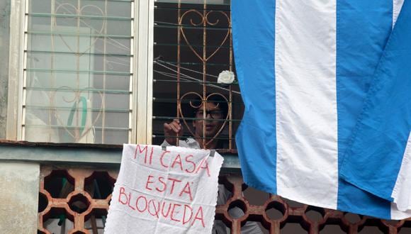 El disidente cubano y líder del movimiento Archipiélago Yunior García mira por la ventana de su departamento con un cartel que dice ``Mi casa está bloqueada'' en La Habana, el 14 de noviembre de 2021. (Foto: AFP)