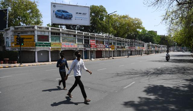 Jóvenes con mascarillas cruzan una calle desierta durante el primer día de bloqueo nacional de 21 días impuesto por el gobierno como medida preventiva contra el coronavirus en Nueva Delhi. (AFP).