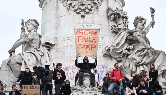 Un hombre sostiene un cartel que dice "Fuera Macron" mientras los manifestantes se paran en la estatua en la plaza Republique durante una manifestación una semana después de que el gobierno impulsara una reforma de las pensiones en el parlamento sin votación, utilizando el artículo 49.3 de la constitución, en París el marzo. 23 de marzo de 2023. (Foto de Emmanuel DUNAND / AFP)