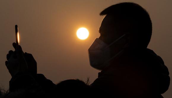 Un hombre que usa una máscara protectora para ayudar a detener la propagación de un virus mortal similar al SARS que se originó en la ciudad central de Wuhan, usa su teléfono celular para tomar una foto de la Ciudad Prohibida en Beijing el 25 de enero de 2020. (Foto de NOEL CELIS/AFP)