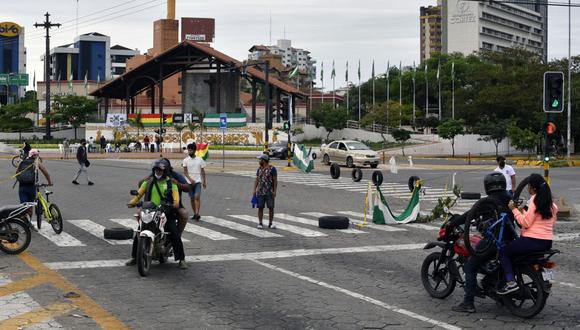 Motociclistas y peatones pasan por una calle bloqueada durante una huelga indefinida convocada por sindicatos opuestos al gobierno del presidente boliviano Luis Arce en Santa Cruz, Bolivia, el 22 de octubre de 2022. (Foto de AIZAR RALDES / AFP)