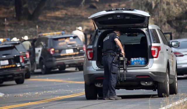 Un oficial de policía agarra un rifle de un vehículo patrulla durante un enfrentamiento con una persona en la zona de incendio evacuada cerca de Lake Berryessa, California. (Foto: EFE / Peter Dasilva).