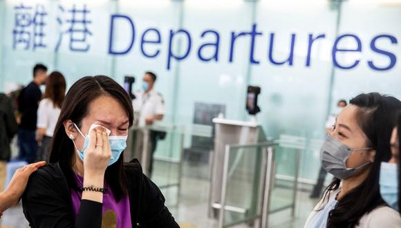 Esta fotografía tomada el 19 de julio de 2021 muestra a una mujer (izquierda) llorando en las puertas de embarque del Aeropuerto Internacional de Hong Kong antes de emigrar a Gran Bretaña. (Foto de ISAAC LAWRENCE / AFP)