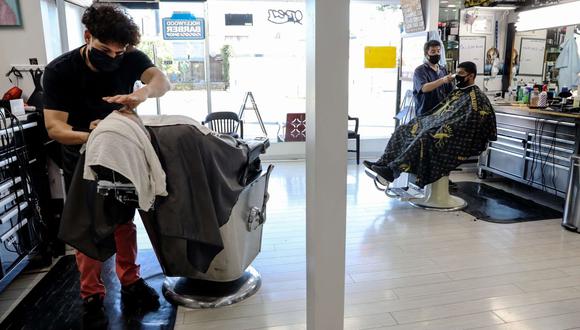 Los barberos usan máscaras faciales mientras trabajan en Hollywood Barber Shop poco antes de cerrar en medio de nuevas restricciones debido a la pandemia de COVID-19. (Mario Tama/AFP).