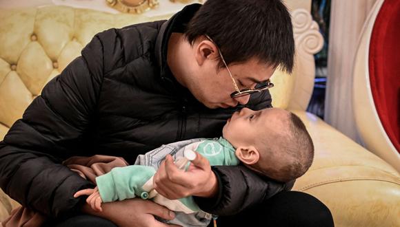 La foto tomada el 21 de octubre de 2021 muestra a Xu Wei sosteniendo a su hijo Xu Haoyang, diagnosticado con síndrome de Menkes, después de extraer orina de su vejiga para analizarla en un hospital, en su casa en Kunming, en la provincia de Yunnan, en el suroeste de China. (Foto de Jade GAO / AFP)