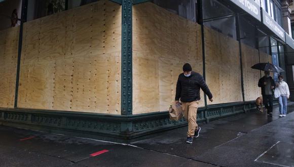 La gente pasa frente a escaparates tapiados como precaución contra posibles daños por protestas electorales en Nueva York. (EFE/JUSTIN LANE).