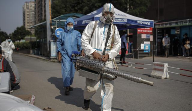 Trabajadores con mascarillas y trajes de protección son vistos mientras realizan operaciones de desinfección en un área residencial de Beijing (China). (EFE/EPA/STRINGER).
