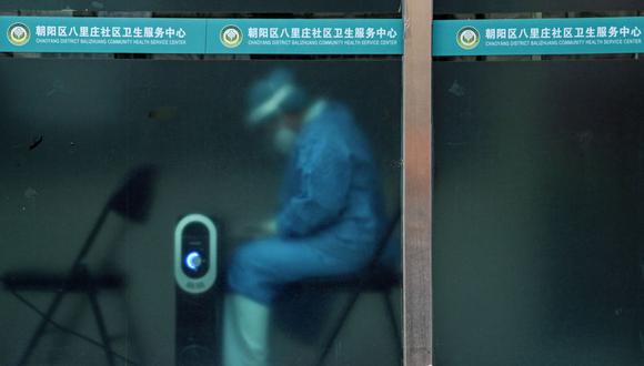 Un trabajador con equipo de protección personal (EPP) se mantiene caliente junto a un calentador cerca de un área residencial cerrada debido a las restricciones del coronavirus Covid-19 en Beijing el 29 de noviembre de 2022. (Foto de Noel CELIS / AFP)