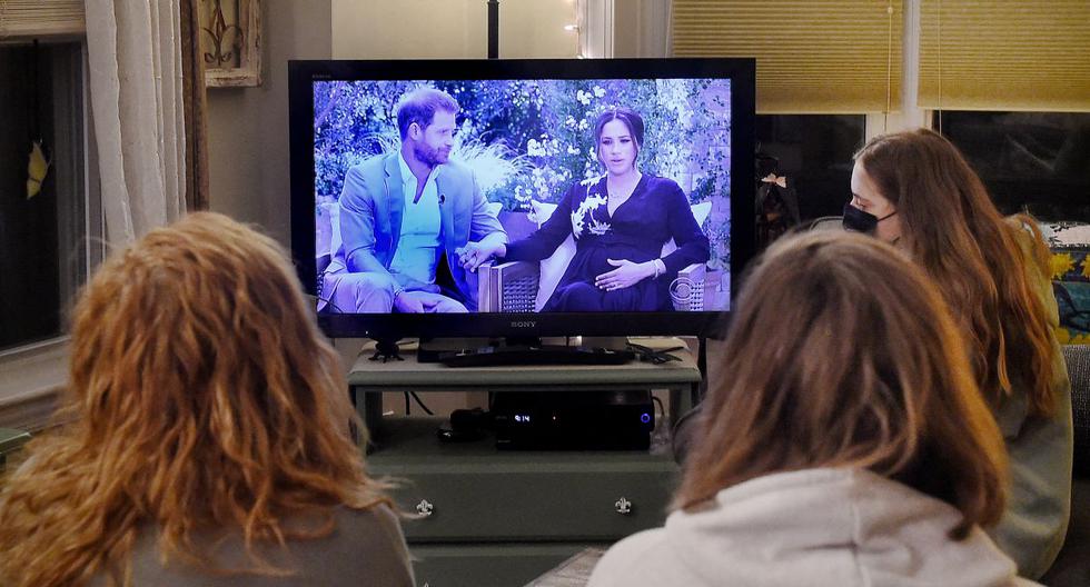 Una familia británica mira la entrevista al príncipe Harry y a su esposa Meghan Markle con la presentadora estadounidense Oprah Winfrey, en Arlington, Virginia, el 7 de marzo de 2021. (Foto de OLIVIER DOULIERY / AFP).