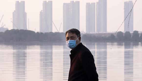 Un hombre usa una máscara facial mientras se encuentra a lo largo de la costa de Wuhan, en la provincia de Hubei. El secretario de Comercio de Estados Unidos indica que este virus es una oportunidad de negocio que dará más empleo a Norteamérica. (Foto: AP)