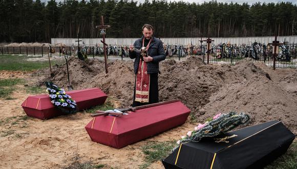Andrii Holovine, sacerdote de la iglesia de San Andrés Pervozvannoho Todos los Santos, dirige el funeral de tres víctimas muertas, en un cementerio de Bucha, el 18 de abril de 2022, durante la invasión rusa de Ucrania. (Foto: Yasuyoshi CHIBA / AFP)