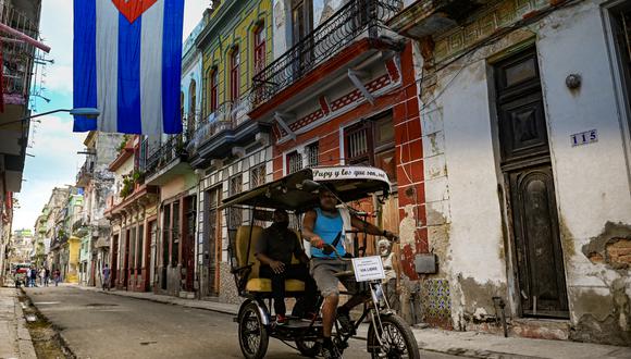 Un bicitaxi circula por una calle decorada con una enorme bandera cubana en La Habana, el 27 de octubre de 2021. (Foto de YAMIL LAGE / AFP)