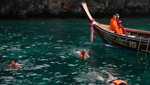 Monjes budistas descansando en un bote de cola larga mientras los turistas bucean en Maya Bay en la isla Phi Phi Leh de Tailandia. (Foto de Lillian SUWANRUMPHA / AFP)