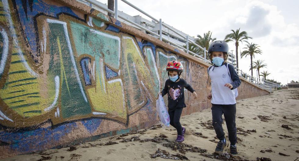 Imagen referencial. Dos niños con máscaras faciales juegan en la playa de Portixol en Palma de Mallorca, el 26 de abril de 2020. (JAIME REINA / AFP).