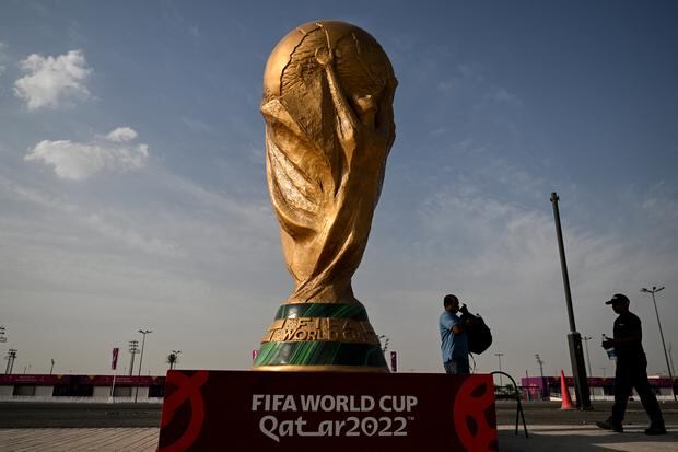 Los hombres pasan frente a una réplica del trofeo de la Copa Mundial de la FIFA fuera del estadio Ahmed bin Ali en Al-Rayyan el 12 de noviembre de 2022, antes del torneo de fútbol de la Copa Mundial de la FIFA Qatar 2022. (Foto de Kirill KUDRYAVTSEV / AFP)