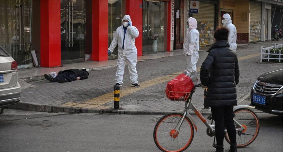 Funcionarios de salud chinos con trajes protectores que verificaron el cuerpo de un hombre con una máscara facial que se derrumbó y murió en una calle cerca de un hospital en Wuhan. (AFP)