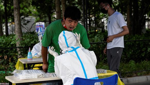 Un trabajador de la salud toma una muestra de hisopo de un hombre para realizarle la prueba del coronavirus Covid-19 en un sitio de prueba improvisado en Beijing el 21 de junio de 2022. (Foto de Jade GAO / AFP)