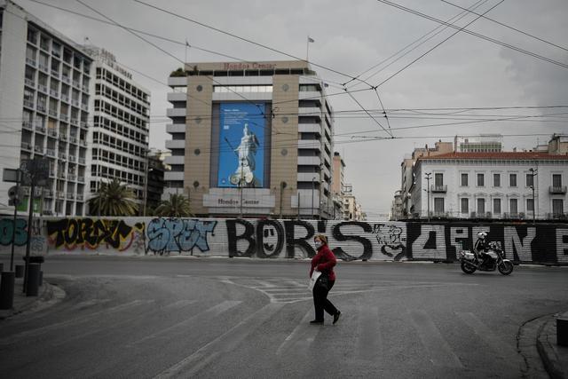 Una mujer que usa una máscara facial para tomar medidas de protección cruza una calle vacía en el centro de Atenas mientras el país lucha por controlar la propagación del COVID-19. (Foto: AFP)