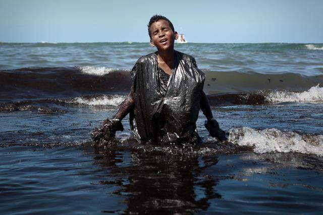 Un niño sale del mar mientras extrae el petróleo derramado en la playa de Itapuama, ubicada en la ciudad de Cabo de Santo Agostinho, estado de Pernambuco, Brasil, el 21 de octubre de 2019. - Grandes gotas de petróleo que manchan más de 130 playas en el noreste de Brasil comenzaron a aparecer a principios de septiembre y ahora han aparecido a lo largo de un tramo de 2.000 km de la costa atlántica. La fuente de los parches sigue siendo un misterio a pesar de las afirmaciones del presidente Jair Bolsonaro de que provienen de fuera del país y posiblemente fueron obra de delincuentes. (Foto de LEO MALAFAIA / AFP)