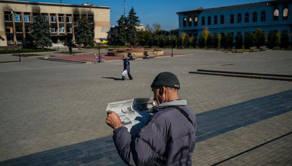 Un residente local leyendo un periódico mientras espera recibir un paquete de alimentos en la plaza central de la ciudad de Izyum, en medio de la invasión rusa de Ucrania. (Foto de Dimitar DILKOFF / AFP)