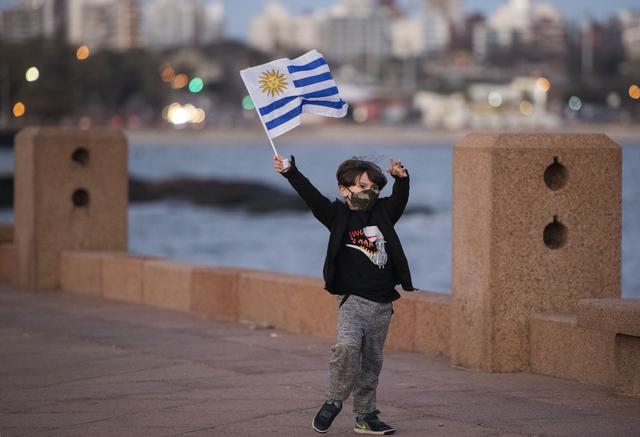 Un niño con una mascarilla ondea una bandera nacional uruguaya mientras juega en el paseo marítimo de Montevideo. (Foto: AP)