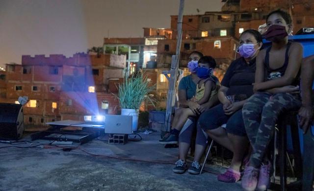 Grandes y chicos disfrutan de la proyección de una película en los techos de Petare, una de las favelas más grandes y peligrosas de Venezuela. (EFE/ Rayner Pena R)