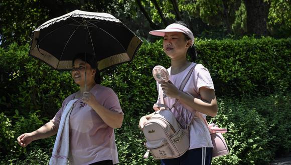 Una mujer que sostiene un paraguas (izquierda) camina con una mujer que usa un ventilador eléctrico portátil durante un clima caluroso en la isla de Gulangyu en Xiamen, en la provincia de Fujian, en el sur de China, el 24 de julio de 2022. (Foto de Jade Gao / AFP)