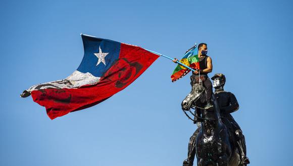 Un manifestante agita una bandera indígena chilena y otra mapuche desde lo alto del monumento General Baquedano en la Plaza Italia durante una protesta contra el gobierno del presidente chileno Sebastián Piñera. (Foto: AFP)
