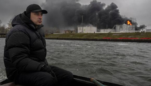 Un pescador navega en su bote por el río Dnipro mientras se eleva humo negro después de un ataque a una reserva de petróleo en Kherson, el 20 de noviembre de 2022, en medio de la invasión rusa de Ucrania. (Foto de BULENT KILIC / AFP)