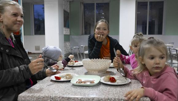 La refugiada ucraniana Swetlana, de 27 años, come con sus hijos y su joven vecino en el antiguo orfanato, que ahora se utiliza como campo de refugiados, en Kryvyi Rig, al sur de Ucrania, el 25 de octubre de 2022, en medio de la invasión rusa de Ucrania. (Foto de BULENT KILIC / AFP)