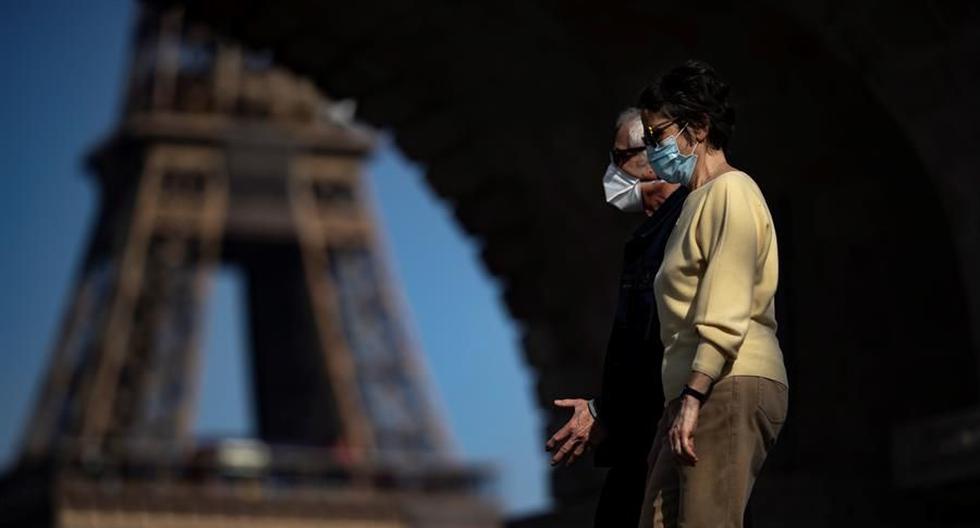 Dos peatones que usan mascarillas protectoras contra el coronavirus disfrutan del cálido clima primaveral mientras cruzan el puente Bir Hakeim, cerca de la Torre Eiffel, en París, Francia. (EFE / EPA / IAN LANGSDON).
