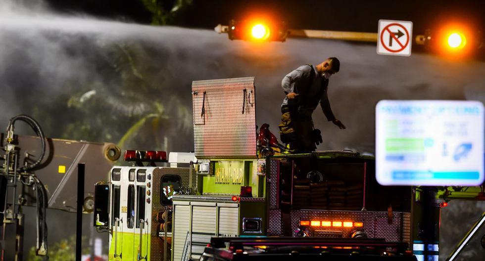 Se ve a un bombero de Miami-Dade trabajando sobre un camión mientras se rocía agua sobre los escombros de un edificio parcialmente derrumbado en Surfside, al norte de Miami Beach, el 25 de junio de 2021. (Eva Marie UZCATEGUI / AFP).