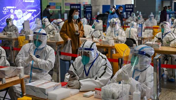 Trabajadores de la salud esperan para hacer la prueba del coronavirus Covid-19 a los pasajeros después de su llegada a la estación de tren de Hongqiao en Shanghái, el 6 de diciembre de 2022. (Foto de Hector RETAMAL / AFP)
