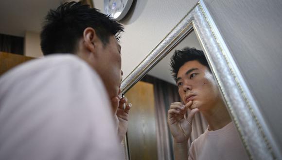 Esta imagen tomada el 22 de julio de 2021 muestra al investigador científico Xia Shurong mirándose en el espejo durante una cita de seguimiento después de su cirugía plástica la semana anterior en una clínica en Beijing. (WANG ZHAO / AFP).