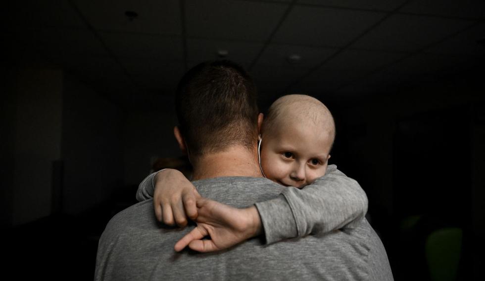 Un adulto sostiene a un niño que lucha contra el cáncer en el sótano del centro de oncología utilizado como refugio antiaéreo, en Kiev el 28 de febrero de 2022. (Foto de Aris Messinis / AFP)