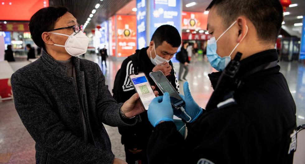Imagen referencial. Pasajero con una máscara facial por el coronavirus muestra un código QR verde en su teléfono para confirmar su estado de salud al oficial de seguridad en China. (AFP / NOEL CELIS).