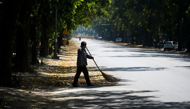 Un hombre que lleva una máscara de protección barre una calle desierta de Nueva Delhi durante el primer día de bloqueo nacional por coronavirus en India. (AFP).