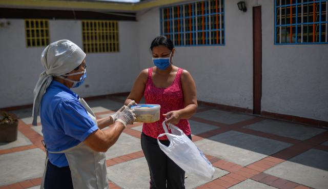 La hermana religiosa Teresa Gómez, de 73 años, le da una comida a una mujer en la guardería Inmaculada Niña de Santa Ana, en el barrio de Casalta, en Caracas. (Federico PARRA / AFP).