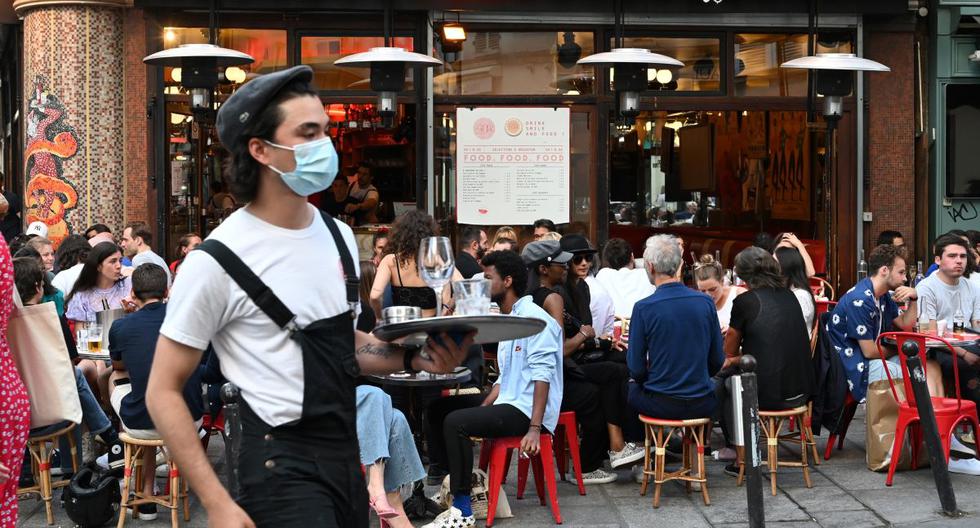 Un mesero que usa mascarilla sirve a los clientes mientras la gente come y bebe en la terraza de un bar en París el 2 de junio de 2020, en plena pandemia de coronavirus. (Foto de BERTRAND GUAY / AFP).