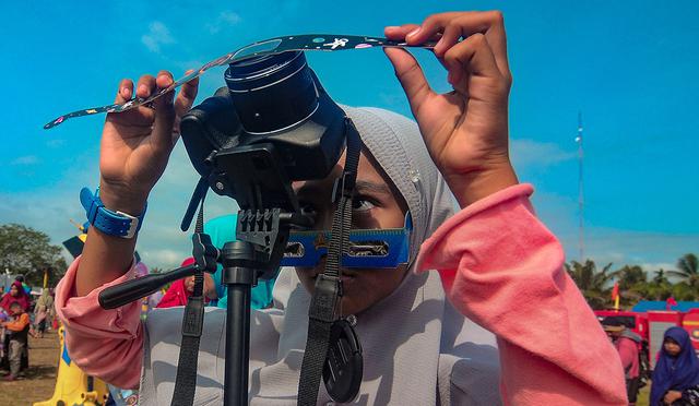 Una niña coloca un filtro frente a su cámara mientras toma fotos de la luna moviéndose frente al sol en un raro eclipse solar de "anillo de fuego" en Siak, provincia de Riau. (Foto: AFP)