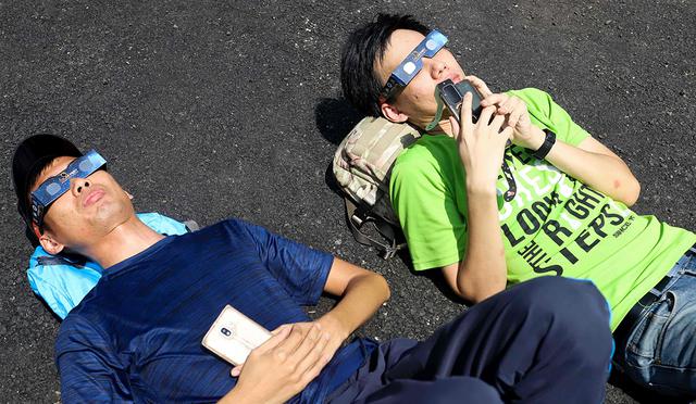 Los visitantes usan lentes de filtro solar para mirar la luna mientras se mueve frente al sol en un raro eclipse solar de "anillo de fuego" en Tanjung Piai, Malasia. (Foto: AFP)